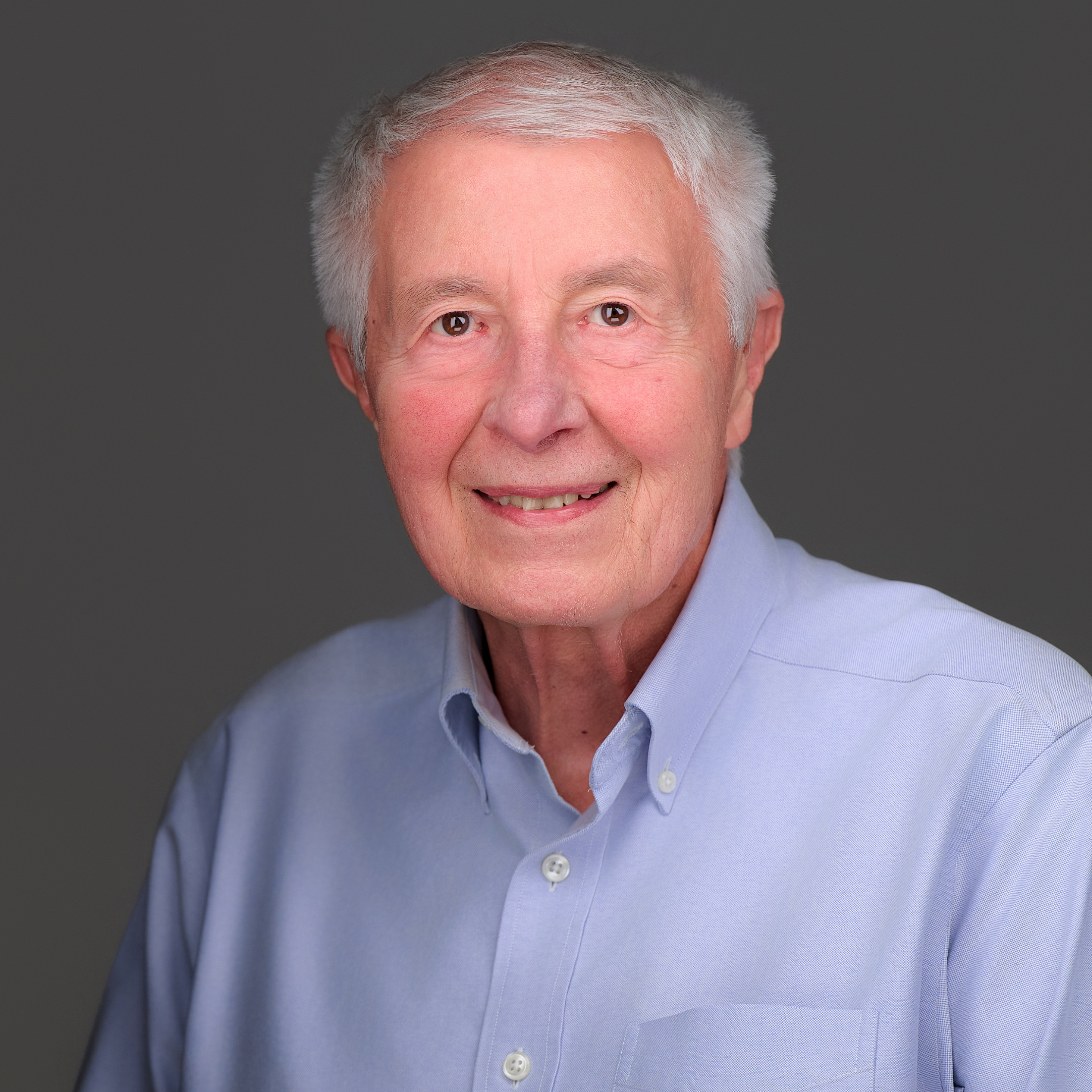 Close-up of Sally Kerschner a VTPHA leadership team member, smiling, she has short grey-black hair, and is wearing a floral top with a back background, a black cardigan and golden hoop earings