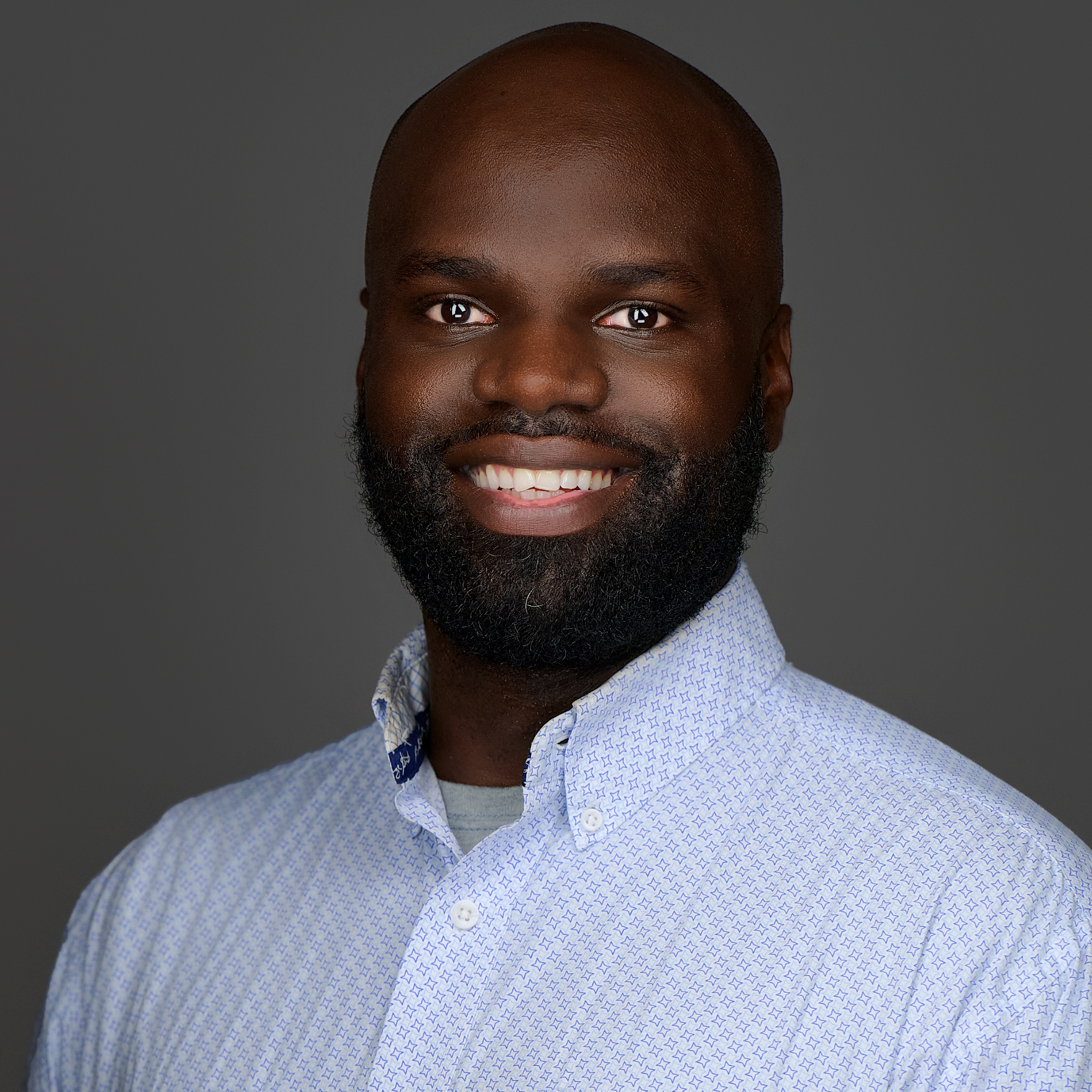 Close-up of Sally Kerschner a VTPHA leadership team member, smiling, she has short grey-black hair, and is wearing a floral top with a back background, a black cardigan and golden hoop earings