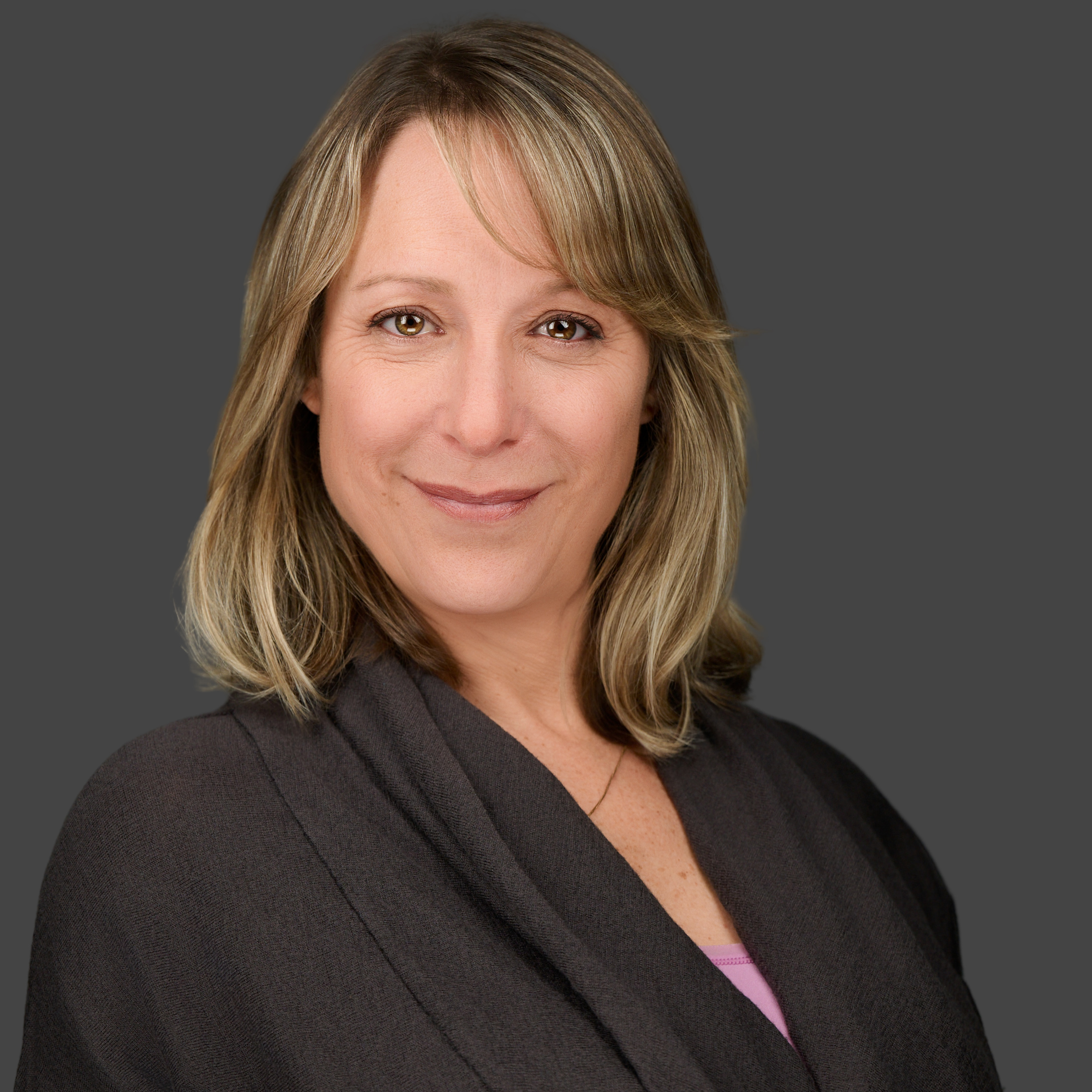 Headshot__Friedman_Color_Cropped Close-up of Sally Kerschner a VTPHA leadership team member, smiling, she has short grey-black hair, and is wearing a floral top with a back background, a black cardigan and golden hoop earings